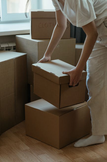 A man and woman inside a room during a home relocation, engaging in a celebratory gesture with their hands. The man, with dark hair tied back, is wearing a dark t-shirt and has a bracelet on his wrist