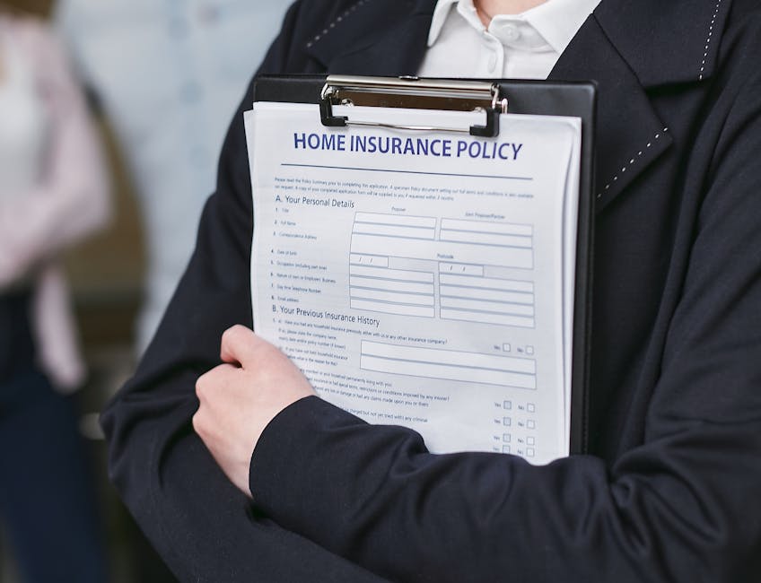 A person dressed in formal business attire holds a clipboard with a 'Home Insurance Policy' form attached, featuring sections for personal details and insurance history. The individual is standing indoors near a doorway, with the clipboard prominently displayed in the foreground. The background is slightly blurred, suggesting a professional environment. This scene relates to property documentation often involved in house removals or relocation planning, which [COMPANY_NAME], such as Man With a Van Harlington, may coordinate as part of their furniture transport and home relocation services. The image emphasizes the importance of insurance and proper documentation during moving and packing processes, highlighting the logistical considerations involved in professional removals.